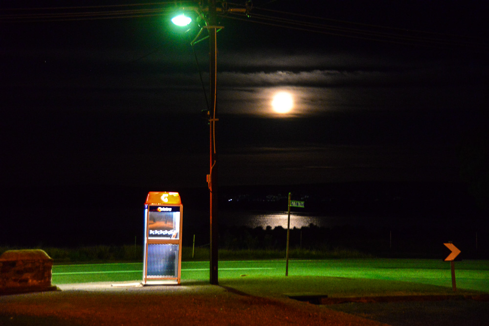 The full moon rises over the Pink Lake in Lochiel next to a Telstra Phone Box.