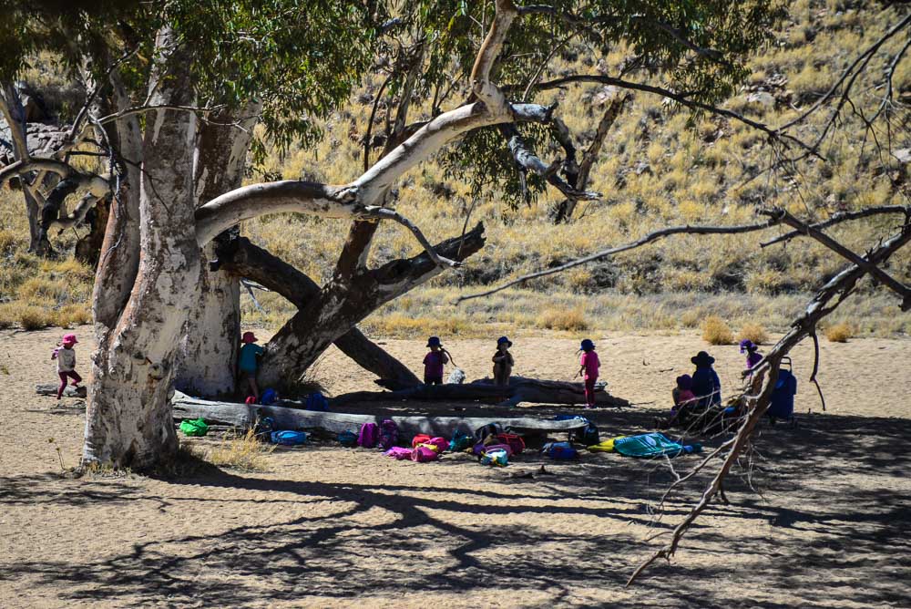 An image of children in the shade of a tree in the dry river bed at Simpsons Gap.